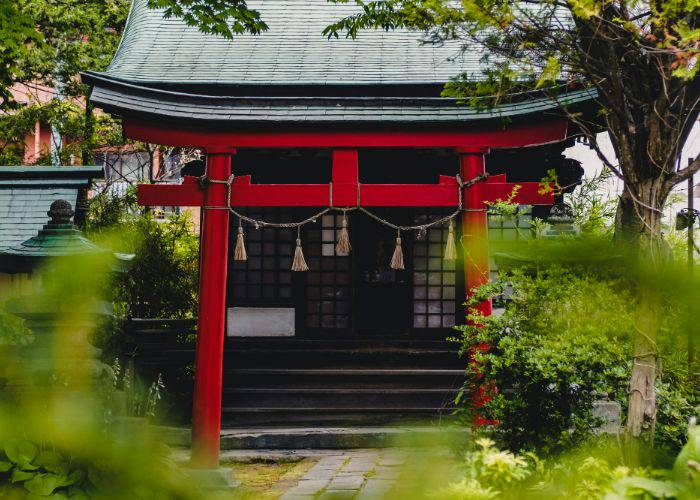 A red Japanese torii gate in front of a Japanese temple.
